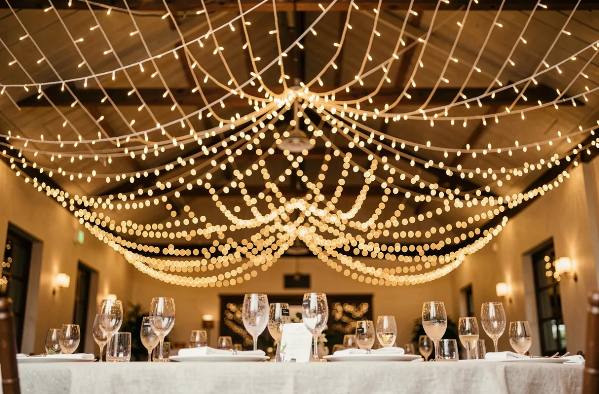 Scénographie lumineuse de mariage avec des guirlandes suspendues au plafond formant un baldaquin lumineux au-dessus des tables de réception